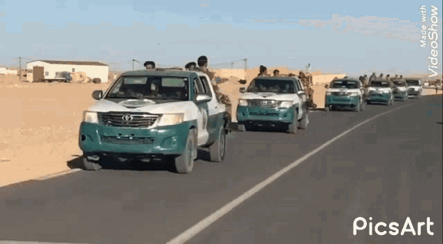 a group of military vehicles are driving down a road in the desert .