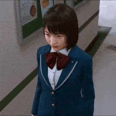 a young girl in a school uniform is standing in a hallway .