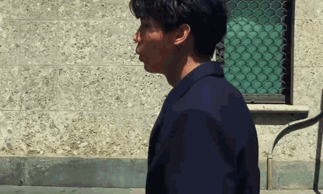 a man in a blue suit is walking in front of a brick wall