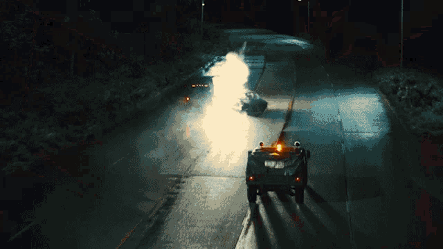 a military vehicle is driving down a highway at night with a car in the background