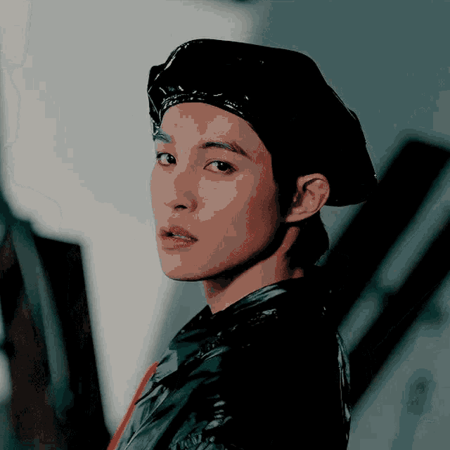 a young man wearing a black beret and a black jacket looks at the camera
