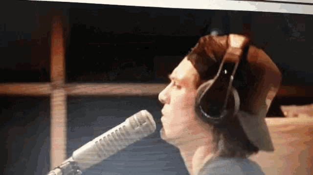 a man wearing headphones and a hat sings into a microphone