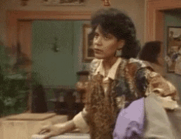 a woman is sitting at a table in a living room holding a purple pillow .