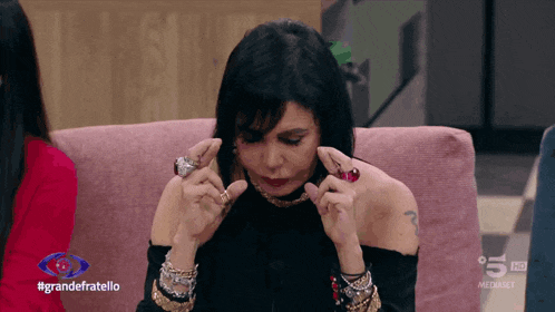 a woman is sitting on a pink couch with the words grandefratello on the bottom