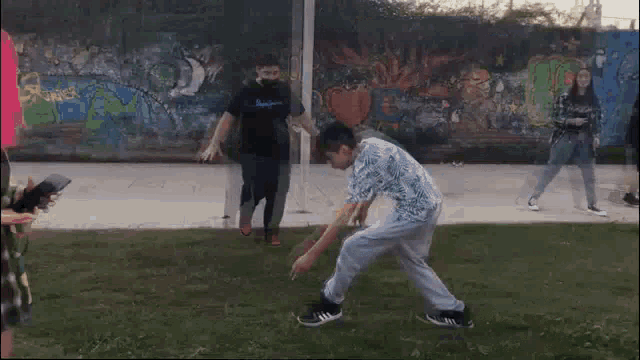 a group of people are dancing in a park in front of a wall with graffiti .