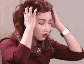a woman in a red shirt is holding her head with her hands .