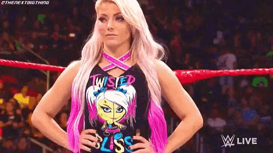 a woman with pink hair and a black shirt is standing in a wrestling ring .