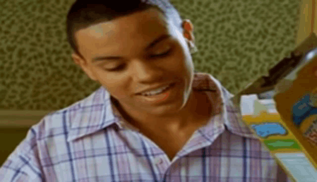 a young man in a plaid shirt is smiling while looking at a box of cereal