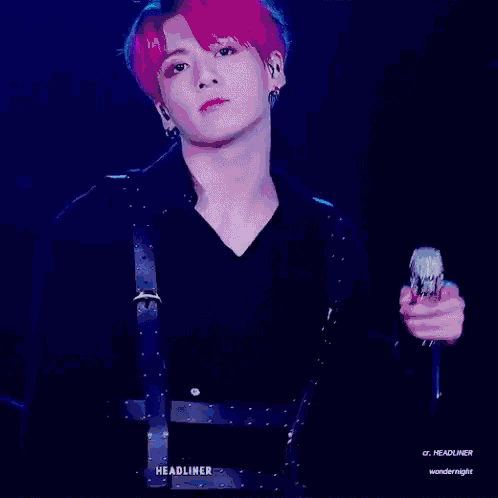 a young man with purple hair is standing in front of a blue background .