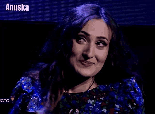 a woman in a blue dress is smiling in front of a screen that says anuska on it