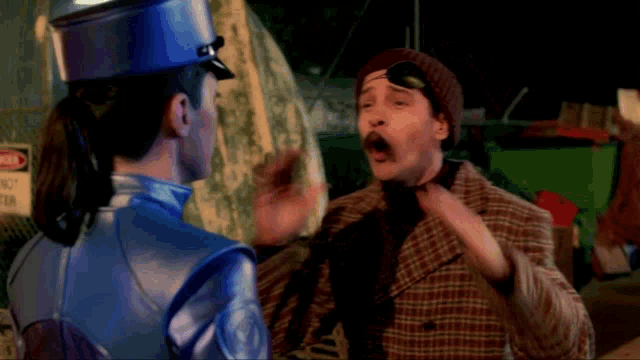 a man in a plaid jacket is talking to a woman in a blue uniform in front of a danger sign