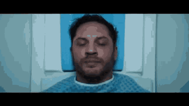 tom hardy is laying in a hospital bed with his eyes closed and a beard .