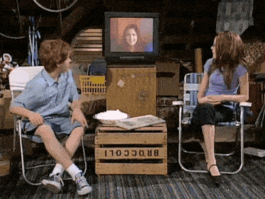 a boy and a girl are sitting in front of a tv and a box that says broccoli on it