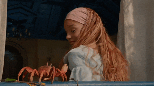 a girl with long red hair looks at a crab