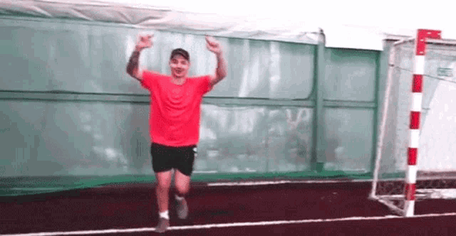 a man in a red shirt and black shorts is running on a soccer field with his arms in the air .
