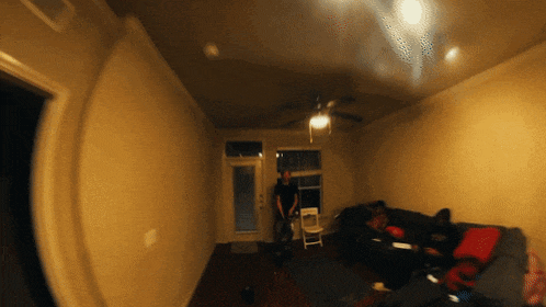 a living room with a ceiling fan and a few people sitting on a couch