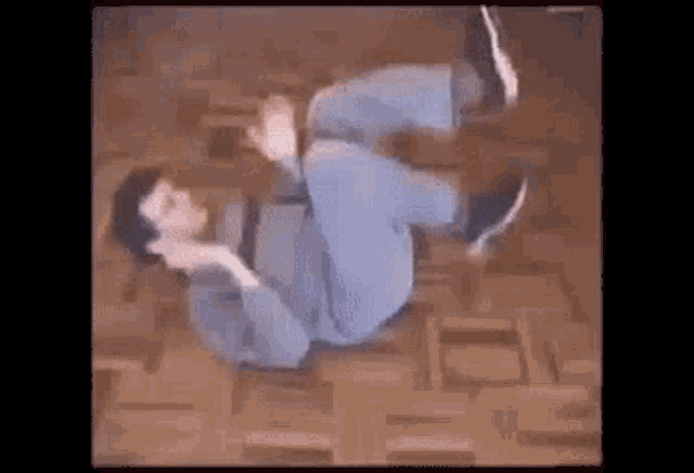 a man is laying on his back on a wooden floor doing a trick .