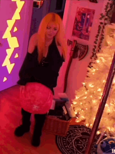 a woman with red hair is standing in front of a christmas tree holding a pink purse .