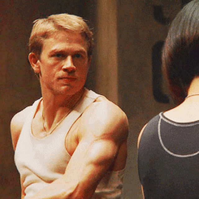 a man in a white tank top is looking at a woman in a black tank top