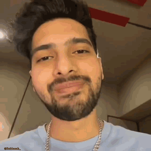 a man with a beard wearing a blue shirt and a silver chain .