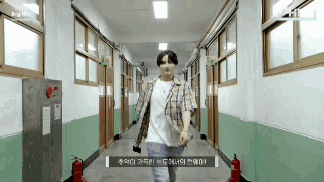 a man in a plaid shirt is walking down a hallway with a fire extinguisher on the right