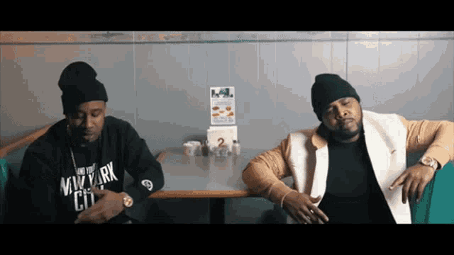 two men sit at a table with one wearing a sweatshirt that says nyc city