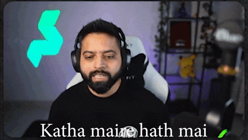 a man with a beard wearing headphones is sitting in front of a screen that says katha mai hath mai