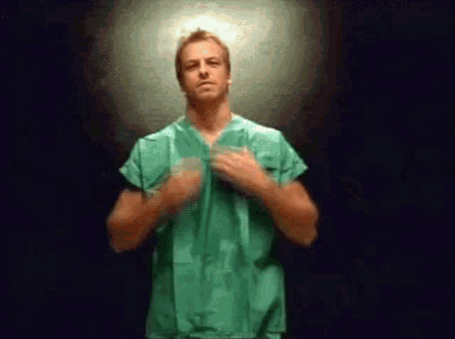 a man in a green scrub top is standing with his hands on his chest .