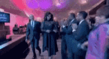 a woman in a black dress is walking through a crowd of people in a room .