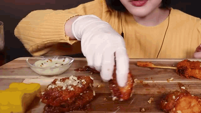 a woman wearing a yellow sweater and white gloves is eating fried chicken .