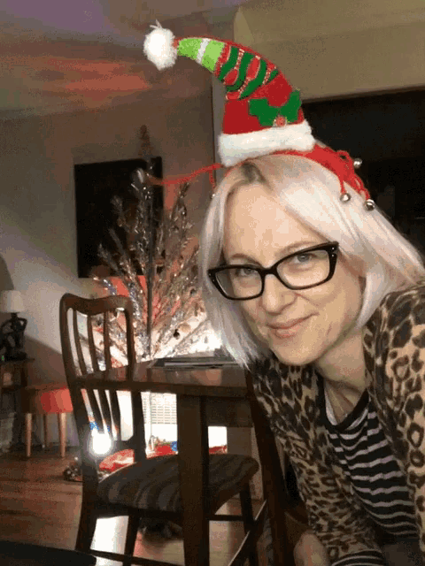 a woman wearing glasses and a santa hat looks at the camera