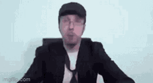 a man in a suit and tie is sitting in a chair and making a funny face .