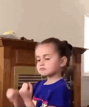 a little girl in a blue shirt is making a funny face while holding her fist in the air .