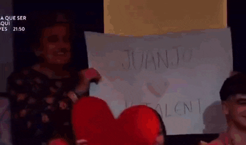 a woman is holding a heart shaped pillow and a sign that says juanjo .