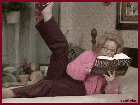 a woman is laying on a bed reading a book titled wars and peace .