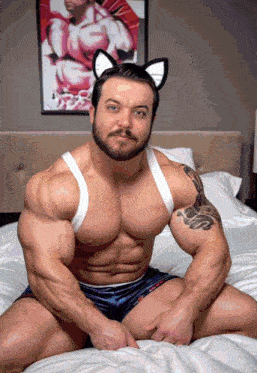 a man wearing cat ears sits on a bed in front of a picture of a man