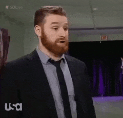 a man with a beard and a suit and tie is standing in a room .