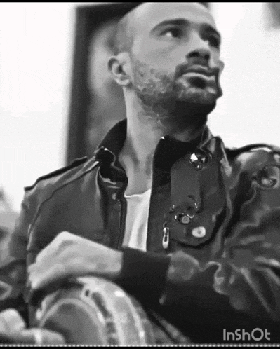a man with a beard is wearing a leather jacket and playing a drum .