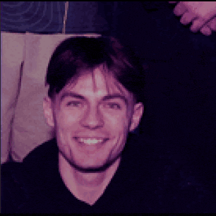 a man with red hair and glasses is smiling in a dark room