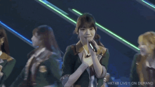 a girl is singing into a microphone while another girl stands behind her .