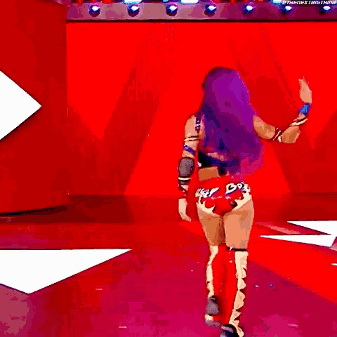 a woman with purple hair is standing in front of a red wall while a man holds her leg .