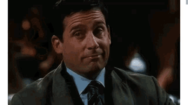 a man in a suit and tie is holding a drink in his hand and making a funny face .