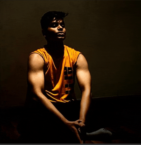 a man wearing a yellow tank top with the letter e on it sits on the floor