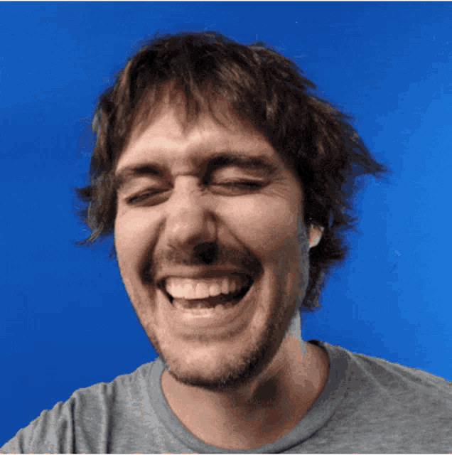 a man with a beard is smiling with his eyes closed against a blue background