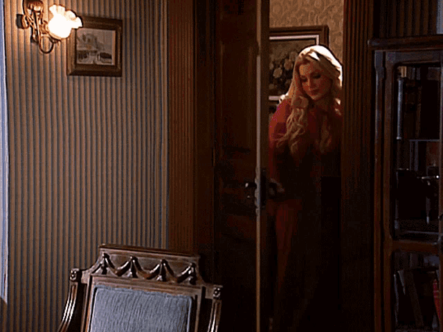 a woman in a red dress stands in a room with striped wallpaper