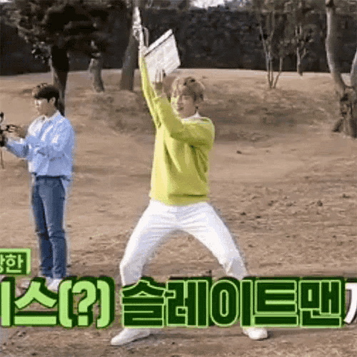 a man in a yellow sweater and white pants is standing on his knees in a field holding a camera .