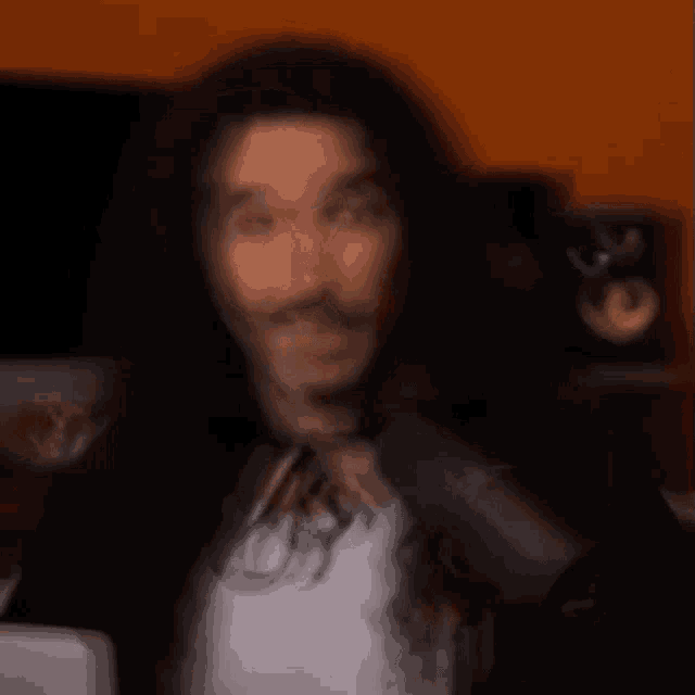 a blurry picture of a man with long hair and a mustache in front of a microphone .