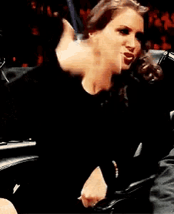 a woman in a black top is sitting in a chair with her hand on her chest