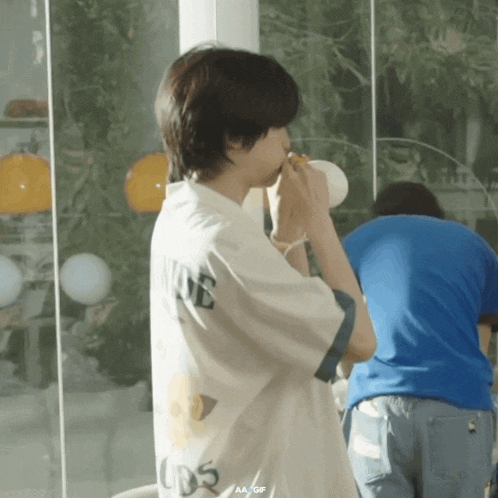 a person wearing a white shirt with the word nine on it is drinking from a cup