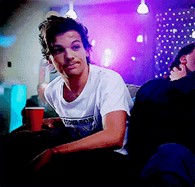 a man sitting on a couch with a red cup and a shirt that says ' sonic boom ' on it